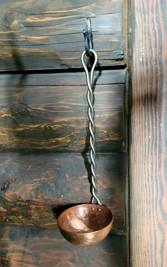 Copper ladle with twisted handle hanging on wooden wall for kitchen use