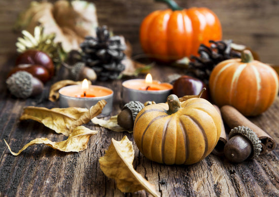 Cozy autumn scene with pumpkins, candles, pinecones, and fallen leaves on rustic wood