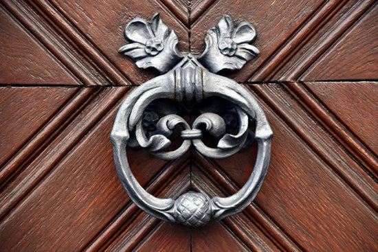 Intricate iron door knocker on wooden door with rustic detailing and floral accents