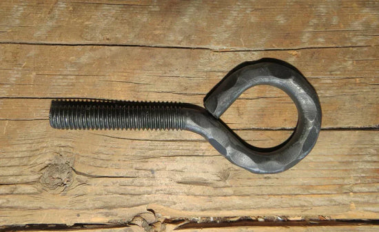 Hammered eye bolt with threaded shaft, resting on rustic wooden surface from Old West Iron