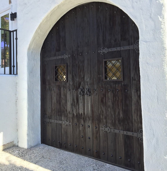 Rustic wooden arch door with decorative iron hardware and diamond-shaped windows